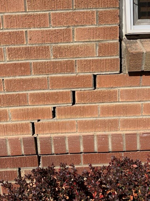 Stair-step settlement cracks beside a window in a brick wall
