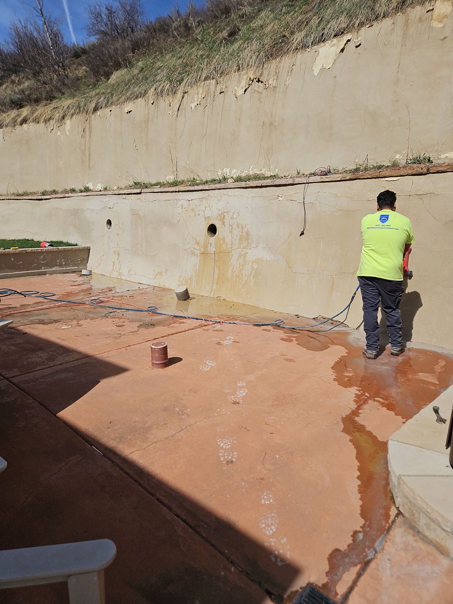 Cracked retaining wall with water staining and new weep holes cut through the face