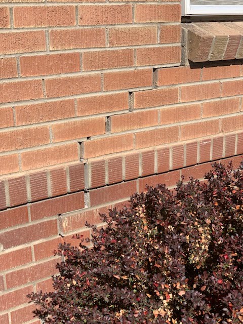 Settlement cracks stepping through brick below a window sill