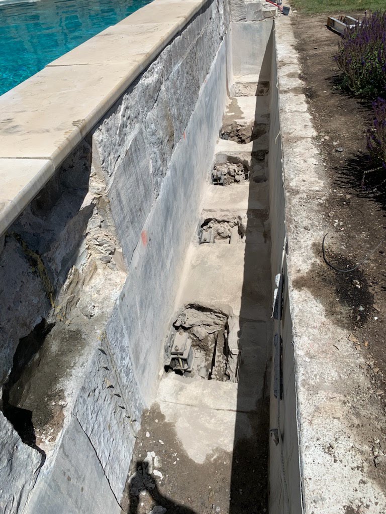 Excavated trench exposing pier locations along a pool foundation wall