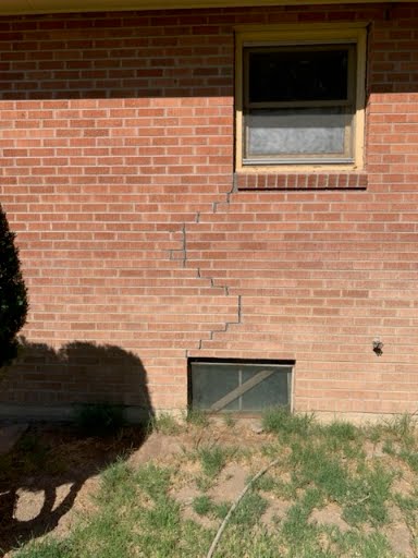 Stair-step foundation crack running through brick below a window