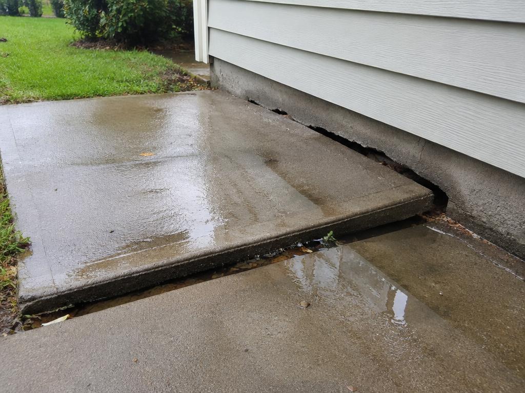 Sidewalk slab tilted toward the house with a gap and pooling water